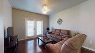 Located at 501 S Loop 250 Frontage Rd W in Midland, Texas, this single-floor residence offers a well-designed layout with functional living spaces and consistent finishes throughout. The living room serves as the heart of the home, featuring rich hardwood flooring, a ceiling light fixture, and French doors fitted with blinds that allow for natural light and outdoor access. The kitchen is outfitted with dark espresso cabinetry, granite-style countertops, and black appliances including a range with over-the-range microwave, providing a practical and cohesive cooking space. The primary bedroom features plush carpeting, dual windows that invite natural light, and ample room for a full furniture arrangement. A second bedroom also offers carpeted flooring with a window view, while a third bedroom accommodates two twin beds and includes a ceiling fan. Both bathrooms are finished with large-format tile flooring, dark vanity cabinetry, and a tub-shower combination. One bathroom connects directly to the primary bedroom, functioning as an en-suite. Throughout the residence, neutral wall tones and consistent wood-toned accents create a cohesive and comfortable atmosphere suited for everyday living.