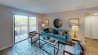 This single-floor residence offers a thoughtfully arranged layout that connects the main living areas in an open, flowing manner. The living room is bright and inviting, featuring wood-look flooring, a textured ceiling, and a large sliding glass door that leads to a private balcony, allowing natural light to fill the space. The area transitions seamlessly into a dedicated dining space, accommodating a full dining set beneath warm overhead lighting.

The galley-style kitchen is well-equipped, featuring dark espresso cabinetry with modern hardware, granite-style countertops, a tile mosaic backsplash, black appliances including a range and refrigerator, and a convenient built-in pantry with open shelving. A breakfast bar connects the kitchen to the main living area.

Both bedrooms are generously sized, finished with plush carpet, neutral-toned walls, and textured ceilings. Each room includes a walk-in closet and windows dressed with blinds and curtain panels. The two full bathrooms each feature a tub-shower combination, wood-look flooring, and a vanity with granite-style countertops and dark wood cabinetry.
