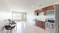 Located at 2141 S Robinson Ave in Milwaukee, WI, this well-appointed one-bedroom, one-bathroom unit offers a thoughtfully designed single-floor layout. The open-concept living area seamlessly connects the kitchen and dining space, creating a bright and functional hub for daily living. Light wood-tone flooring runs throughout the main area, complemented by neutral gray walls and large windows that invite abundant natural light.

The kitchen is outfitted with rich dark-wood cabinetry extending to the ceiling for generous storage, light-toned countertops, and a full suite of stainless steel appliances including a refrigerator, range, microwave, and dishwasher. The adjacent dining area offers an airy, open feel with room to accommodate a dining set comfortably.

The bedroom features plush carpet flooring, soft neutral tones, and a window with views of the surrounding Milwaukee skyline and greenery. A dedicated closet provides additional storage.

The bathroom is finished with tile flooring, a single-sink vanity with dark wood cabinetry and a white countertop, a large mirror, and a walk-in shower. A convenient in-unit laundry closet houses a stacked washer and dryer alongside wire shelving for added organization. The hallway connects all rooms efficiently, completing this clean, modern, and move-in-ready space.
