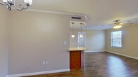 This single-floor residence offers a well-designed layout with consistent wood-look flooring running throughout the main living areas and bedrooms, complemented by clean white crown molding that adds a polished finish to each room. The kitchen is thoughtfully equipped with warm honey-toned cabinetry, granite countertops, a stainless steel sink, a dishwasher, a refrigerator, and a tile backsplash with a classic diamond pattern. A peninsula with a rich wood base and granite top serves as a natural divider between the kitchen and the adjacent dining area, which features an elegant chandelier overhead. The open living area benefits from natural light filtering through multiple windows. The dining space connects seamlessly to the main living zone, creating an easy flow for everyday living and entertaining. The bedrooms are generously proportioned, each with wood-look flooring, crown molding, ceiling fans, and windows that bring in natural light. A walk-in closet provides ample storage with built-in shelving and hanging rods. The bathroom includes a full-sized soaking tub with a tiled surround and chrome fixtures, offering a clean and functional design. The overall ambiance is bright, neutral, and move-in ready.