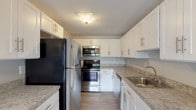 This single-floor residence offers a clean, neutral aesthetic with a practical and comfortable layout. The galley-style kitchen is a standout feature, outfitted with stainless steel appliances including a refrigerator, electric range, built-in microwave, and dishwasher. White shaker-style cabinetry provides ample storage, complemented by granite-look countertops and light wood-look flooring that lends a modern touch to the space.

The living area is generously sized, featuring plush wall-to-wall carpeting, soft gray walls, and large windows fitted with blinds that allow for an abundance of natural light. A sliding glass door provides additional light and outdoor access, while a pendant light fixture adds a subtle decorative element.

Multiple bedrooms continue the consistent design language of the home, each carpeted and finished with the same soft gray palette. The bedrooms are well-lit by windows overlooking greenery, and at least one bedroom includes a built-in closet with double doors for convenient storage.

The bathroom is finished with light tile flooring, a white vanity with storage cabinetry, a mirrored medicine cabinet, and a combined tub and shower enclosure. The overall design of the residence is cohesive, understated, and move-in ready.
