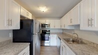 This single-floor residence offers a clean, neutral aesthetic with a practical and comfortable layout. The galley-style kitchen is a standout feature, outfitted with stainless steel appliances including a refrigerator, electric range, built-in microwave, and dishwasher. White shaker-style cabinetry provides ample storage, complemented by granite-look countertops and light wood-look flooring that lends a modern touch to the space.

The living area is generously sized, featuring plush wall-to-wall carpeting, soft gray walls, and large windows fitted with blinds that allow for an abundance of natural light. A sliding glass door provides additional light and outdoor access, while a pendant light fixture adds a subtle decorative element.

Multiple bedrooms continue the consistent design language of the home, each carpeted and finished with the same soft gray palette. The bedrooms are well-lit by windows overlooking greenery, and at least one bedroom includes a built-in closet with double doors for convenient storage.

The bathroom is finished with light tile flooring, a white vanity with storage cabinetry, a mirrored medicine cabinet, and a combined tub and shower enclosure. The overall design of the residence is cohesive, understated, and move-in ready.
