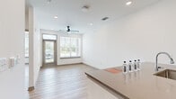 Located at 101 Dean Ave in Raymore, MO, this efficiently designed one-bedroom, one-bathroom unit offers a clean, modern aesthetic across a single floor. The open-concept living and kitchen area creates a seamless flow, anchored by a central island with a quartz-style countertop, undermount sink, and generous prep space. The kitchen features light wood cabinetry, a white subway tile backsplash, and a full suite of stainless steel appliances including a French door refrigerator, electric range, and over-the-range microwave. Light-toned luxury vinyl plank flooring runs throughout the entire unit, lending a cohesive, contemporary feel. The living area benefits from a ceiling fan and large windows with blinds that invite ample natural light and outdoor views. The bedroom is a well-proportioned private retreat with dual windows, a ceiling fan, and a double-door closet offering plentiful storage. The bathroom is outfitted with a wood-tone vanity, quartz countertop, framed mirror, and overhead lighting, maintaining the unit's consistent modern design language. Clean white walls and recessed lighting throughout contribute to a bright, welcoming ambiance.