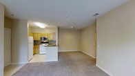 Located at 8800 Cattle Creek Pl in Raleigh, NC, this single-story space features an open-concept design that seamlessly connects the kitchen and living area. The kitchen is equipped with light wood cabinetry, a tile backsplash, stainless steel microwave, white range, and a full-size refrigerator. A peninsula counter provides a natural transition between the kitchen and the adjoining living space, making it ideal for both meal preparation and casual dining. The flooring transitions from smooth tile in the kitchen to plush carpeting throughout the living area, adding warmth and comfort underfoot. Recessed lighting and a flush-mount ceiling fixture provide consistent illumination throughout the space. The living area is generously sized with neutral-toned walls that offer versatility for a variety of furnishing styles. HVAC vents integrated into the ceiling ensure climate control throughout. The overall layout is practical and efficient, making good use of the available space while maintaining an open, airy feel.