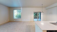 Located in Edgewood, WA, this single-floor, 3-bedroom, 2-bathroom unit offers a well-organized layout that maximizes functionality. The open kitchen is a standout feature, equipped with dark wood-grain cabinetry extending to the upper walls, white countertops, black appliances including a range and refrigerator, and wood-style flooring. A peninsula with a built-in sink doubles as a breakfast bar, seamlessly connecting the kitchen to the carpeted living area, which is accented by track lighting and a pendant light. The bedrooms are carpeted and bathed in natural light through blinds-fitted windows, each equipped with baseboard heating. The primary bedroom includes a closet with sliding doors. A carpeted hallway connects the bedrooms and both bathrooms. The bathrooms feature white tub-shower combinations and vanities with wide mirrors and light fixtures. An in-unit laundry room houses a full-size GE washer and dryer with overhead wire shelving for additional storage. A dedicated pantry or storage closet with built-in shelving adds further practicality. Neutral tones and consistent finishes throughout create a clean, cohesive ambiance.