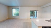 Located in Edgewood, WA, this single-floor, 3-bedroom, 2-bathroom unit offers a well-organized layout that maximizes functionality. The open kitchen is a standout feature, equipped with dark wood-grain cabinetry extending to the upper walls, white countertops, black appliances including a range and refrigerator, and wood-style flooring. A peninsula with a built-in sink doubles as a breakfast bar, seamlessly connecting the kitchen to the carpeted living area, which is accented by track lighting and a pendant light. The bedrooms are carpeted and bathed in natural light through blinds-fitted windows, each equipped with baseboard heating. The primary bedroom includes a closet with sliding doors. A carpeted hallway connects the bedrooms and both bathrooms. The bathrooms feature white tub-shower combinations and vanities with wide mirrors and light fixtures. An in-unit laundry room houses a full-size GE washer and dryer with overhead wire shelving for additional storage. A dedicated pantry or storage closet with built-in shelving adds further practicality. Neutral tones and consistent finishes throughout create a clean, cohesive ambiance.