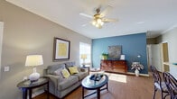 This single-story, 2-bedroom, 2-bathroom unit offers a well-organized layout across a modest but efficiently utilized floor plan. The living room serves as the central gathering space, featuring wood-look flooring, crown molding, a ceiling fan with light fixture, and multiple windows with horizontal blinds that allow generous natural light. A bold accent wall in deep blue-gray adds visual interest, complementing the neutral taupe walls throughout.

The kitchen is designed in a galley-style configuration, equipped with light wood cabinetry, white appliances including a range, microwave, and refrigerator, and a peninsula with bar-height seating for three—creating a seamless connection to the main living area. Wood-look flooring continues throughout the kitchen.

The primary bedroom offers carpeted flooring, tall ceilings, and a walk-in closet, while the second bedroom also features carpet, a standard closet, and a large window providing ample natural light.

Both bathrooms follow a consistent design with white vanity cabinetry, single-sink countertops, large mirrors, and a tub-shower combination. One bathroom features warm wood-look flooring, while both maintain a clean, functional aesthetic with ample under-sink storage.