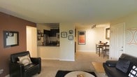 Located at 4957 S. Prince Ct. in Littleton, Colorado, this single-floor residence offers a thoughtfully designed open-concept layout that seamlessly connects the main living areas. The living room provides a comfortable and welcoming atmosphere, featuring plush carpeting, recessed track lighting, and ample space for seating and relaxation. A textured ceiling adds a classic touch throughout the home. The kitchen is positioned adjacent to the living area and is accessible via a pass-through counter, making it ideal for entertaining. It is equipped with dark cabinetry, a stainless steel refrigerator, and a sink overlooking the open space. Track lighting illuminates the kitchen workspace efficiently. The dining area sits just off the kitchen and living room, offering a defined space for meals while maintaining the open flow of the floor plan. Wall art and decorative accents throughout contribute to the warm, lived-in character of the home. The neutral color palette of beige and white walls, combined with the carpeted floors, creates a cohesive and inviting ambiance across the entire single-level layout.