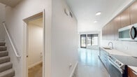 This contemporary two-floor space showcases a clean, modern aesthetic throughout. The open main level features polished concrete floors that reflect natural light, creating a bright and airy atmosphere. Large black-framed windows and a glass door at the front of the living area frame outdoor views while inviting an abundance of daylight into the space.

The galley-style kitchen is well-appointed with warm wood cabinetry extending to the ceiling, crisp white countertops, and a full suite of stainless steel appliances including a range, over-the-range microwave, and refrigerator. A white tile backsplash completes the clean, contemporary look.

Adjacent to the main living area, a bathroom is accessible from the hallway, offering a double-sink vanity with matching wood cabinetry and white countertops, a full wall mirror, and a combined tub and shower. The bedroom features polished concrete flooring, an exposed concrete ceiling detail adding an industrial character, and direct access to a walk-in closet with built-in shelving.

Throughout the space, white walls, recessed lighting, and consistent material choices create a cohesive and minimalist design. The two-floor layout provides a well-organized flow, making this a functional and stylish modern space.