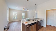 This single-floor residence showcases a thoughtfully designed open-concept layout that seamlessly connects the kitchen and living spaces. The kitchen serves as a central hub, featuring dark espresso cabinetry, granite countertops, and a peninsula with an undermount double sink and stainless steel dishwasher. Pendant lighting hangs above the peninsula, complementing the stainless steel appliances, including a range, over-the-range microwave, and refrigerator. Hardwood-style flooring runs throughout the main living areas, adding warmth and continuity.

The living area is bathed in natural light from multiple windows fitted with blinds, and a ceiling fan adds comfort overhead. A separate carpeted room features floor-to-ceiling French doors that open to an outdoor view, offering an inviting, light-filled retreat. The bathroom is well-equipped with dark vanity cabinetry, a dual-sink countertop, tile flooring, and a glass-enclosed shower with tile surround. Throughout the residence, neutral wall tones and clean architectural lines create a cohesive, modern ambiance suited to comfortable everyday living.