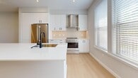 This contemporary 3-bedroom, 4-bathroom residence spans three floors totaling 1,520 square feet, offering a well-organized layout with a 230 sq ft ground floor, 660 sq ft main floor, and 640 sq ft upper floor. The ground level includes a private attached garage with recessed lighting and a roll-up door. The main floor hosts an open-concept kitchen and living area featuring white shaker cabinetry, quartz countertops, a center island, white subway tile backsplash, stainless steel appliances including a gas range and French door refrigerator, and light hardwood flooring throughout. The bathrooms are finished with neutral tile flooring, white vanities with quartz counters, and matte black hardware and fixtures. One bathroom includes a frameless glass walk-in shower with marble-style tile surround. The three bedrooms are bright and airy, each featuring light hardwood floors, soft neutral walls, and window blinds that allow ample natural light. The primary bedroom measures 170 sq ft and is equipped with a ceiling fan. Three staircases connect the floors, supported by two hallways. The home presents a clean, modern aesthetic with a consistent neutral palette and quality finishes throughout.