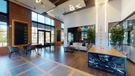 This single-floor amenity space showcases a thoughtfully designed interior that seamlessly blends industrial and contemporary aesthetics. Exposed brick walls, soaring ceilings, and floor-to-ceiling windows flood the space with natural light and offer expansive outdoor views, creating an open, airy atmosphere throughout.

The café area greets visitors near the entrance, featuring large glass doors, warm wood flooring, and casual café-style seating. Adjacent to it, a welcoming lounge area provides comfortable sofas and a reception desk, accented by sculptural pendant lighting in gold tones.

The game and entertainment lounge is anchored by a full-size billiard table set atop speckled dark flooring, surrounded by plush seating arrangements and abundant natural light from oversized windows. Exposed ductwork on the ceiling reinforces the industrial character of the space.

A dedicated café and beverage station features built-in cabinetry with wood-grain finishes, a commercial coffee machine, open shelving with greenery, and a generous counter workspace. Nearby, high-top bistro tables with leather barstools provide casual seating beneath framed artwork.

A more intimate lounge nook offers tufted banquette seating with ambient LED backlighting, a wall-mounted display screen, and elegant marble-topped tables with gold accents. A co-working area provides communal tables, bar-height seating, a backlit display shelf, and large-format artwork, completing this versatile and refined amenity space.