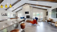 Located at 645 Old Hickory Blvd in Nashville, TN, this single-floor living space offers a thoughtfully designed interior that blends rustic charm with contemporary style. The room is anchored by dramatic vaulted ceilings adorned with rich, dark wood exposed beams that draw the eye upward and lend a sense of grandeur to the space. A floor-to-ceiling stacked stone fireplace serves as a commanding focal point, topped with a wall-mounted flat-screen TV and flanked by a wide concrete hearth. The open layout accommodates multiple distinct seating areas, furnished with vibrant mid-century modern pieces including a tufted royal blue velvet sofa, burnt orange accent chairs, and warm-toned upholstered seating. A full-sized pool table occupies a central position in the space, complementing the social, lounge-like atmosphere. A bar area with pendant lighting, rustic bar stools, and a reclaimed wood accent wall adds to the eclectic, Nashville-inspired character. Large windows throughout flood the interior with abundant natural light and offer views of the surrounding greenery. Light hardwood-style flooring ties the entire space together, creating a warm, inviting ambiance suited for both relaxation and entertainment.