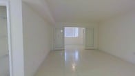 This single-floor space offers a clean, minimalist aesthetic defined by its crisp white walls and smooth tile flooring that runs seamlessly throughout the interior. The open layout creates a sense of spaciousness, with an unobstructed floor plan that lends itself to a variety of uses and configurations. Natural light plays a central role in the ambiance of the space, streaming in generously through a large window fitted with vertical blinds, illuminating the interior with a bright, airy quality. Glass-paneled doors add a modern architectural touch while maintaining visual connectivity between areas, enhancing the overall sense of openness. The ceiling features subtle architectural detailing with gentle recesses, adding dimension to an otherwise streamlined overhead finish. The neutral color palette — consistent across the walls, ceiling, and flooring — creates a cohesive and versatile environment well-suited for professional, retail, or functional use. The transitions between areas are smooth and well-defined, with the glass doors serving as elegant dividers that preserve the flow of light while delineating distinct zones within the space. Overall, the interior presents a polished, well-maintained environment that is both functional and visually inviting.