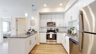 Located at 174 Emery Ave NW in Concord, North Carolina, this single-floor residence offers a thoughtfully designed layout with modern finishes throughout. The entry foyer welcomes you with warm wood-look flooring and louvered closet doors, setting the tone for the clean, contemporary aesthetic found throughout the space.

The kitchen is a standout feature, boasting white shaker-style cabinetry extending to the ceiling, granite countertops, a classic white subway tile backsplash, and a full suite of stainless steel appliances including a range, microwave, dishwasher, and refrigerator. Pendant lighting and a breakfast bar add both style and functionality. The wood-look flooring continues seamlessly from the kitchen into the open living area, which is bathed in natural light from large French doors that invite an airy, welcoming ambiance.

The bedrooms are carpeted for comfort and feature generous windows with views of the surrounding greenery, providing a calm, restful atmosphere. Each bathroom is finished with granite-topped white vanities, wood-look flooring, and tub-shower combinations, maintaining a consistent, polished look throughout. The overall design balances modern style with everyday practicality, creating a comfortable and inviting living environment.