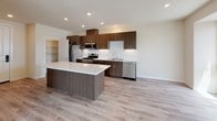 This single-story unit offers a thoughtfully designed open-concept layout that seamlessly connects the living, dining, and kitchen areas. Soaring ceilings in the main living space enhance the sense of openness, while large sliding glass doors flood the interior with natural light and provide direct access to a private balcony overlooking the surrounding community. Light-toned hardwood-style flooring runs throughout the main living areas, contributing to a clean, contemporary aesthetic.

The kitchen is a standout feature, appointed with rich dark wood cabinetry, quartz countertops, a white tile backsplash, and a full suite of stainless steel appliances including a gas range, built-in microwave, refrigerator, and dishwasher. A large center island offers additional prep space and casual seating. A dedicated pantry with built-in shelving provides generous storage.

The bedroom is carpeted for comfort and features a ceiling fan, as well as its own sliding glass door opening to a private balcony. The full bathroom includes a wood-toned vanity with quartz countertop, a large mirror, and a glass-enclosed shower. The overall ambiance is bright, modern, and move-in ready.