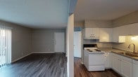 This two-floor residence offers a practical and well-organized layout spread across two levels connected by a staircase. The main level features an open living area finished with dark hardwood-style flooring that extends through the entryway and into the adjacent spaces. A sliding glass door fitted with vertical blinds fills the living room with natural light while providing direct access to an outdoor area. The kitchen is efficiently arranged in an L-shaped configuration, equipped with white cabinetry, laminate countertops, a coil-burner electric range, and a single-basin sink with under-cabinet storage. A full bathroom on this level includes a single-sink vanity with under-cabinet storage, a toilet, and a tub-shower combination, all finished with wood-look flooring and neutral grey walls. The upper level houses the bedrooms, each carpeted and painted in soft grey tones. Both rooms feature ceiling fans with integrated light fixtures and windows that allow natural light to filter in. The dollhouse-view scan confirms a clearly segmented upper floor with carpeted rooms and hardwood-style flooring visible on the lower level. Throughout, textured ceilings, white baseboards, and a consistent neutral palette provide a cohesive and understated aesthetic.