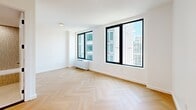 Located at 104 Fleet Pl in Brooklyn, NY, this thoughtfully designed three-bedroom, one-bathroom residence offers a clean, contemporary aesthetic throughout. Signature light oak herringbone parquet flooring runs seamlessly across every room, lending warmth and visual continuity to the entire space.

The generous primary bedroom is bathed in natural light, with expansive floor-to-ceiling windows framing impressive panoramic views of the Brooklyn and Manhattan skylines. The two additional bedrooms also feature large black-framed windows with urban views, along with ample closet storage provided by full-height double-door wardrobes accented with sleek matte black hardware.

The bathroom is elegantly finished with terrazzo-style flooring, vertical mosaic tile walls, and a soaking tub and shower combination enclosed by a glass panel. A wooden vanity with an integrated sink and recessed shelving completes the refined, spa-like atmosphere.

Throughout the residence, crisp white walls and clean architectural lines create a bright, minimalist environment. The black-framed interior doors echo the window detailing, providing a cohesive modern design language. This well-appointed home offers an ideal balance of style, comfort, and striking city views in the heart of Brooklyn.