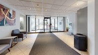 Located at 8 Silver Maple Crt in Brampton, Ontario, this ground-floor lobby space offers a well-appointed and functional entry experience for residents and visitors alike. The space is organized into two distinct zones that work together to create a cohesive and welcoming environment.

Upon entry, floor-to-ceiling glass doors and expansive glazed sidelights flood the foyer with natural light, providing clear sightlines to the outdoor surroundings. The entrance area features a combination of light-toned ceramic floor tiles and a durable carpet runner that guides visitors deeper into the space.

A generous corridor extends through the heart of the lobby, finished with the same tile-and-carpet flooring combination and lined with drop-panel ceilings fitted with recessed lighting. The walls are adorned with colorful, large-format artwork that adds warmth and visual interest to the otherwise clean, neutral palette of whites and soft grays.

One side of the lobby houses an extensive bank of smart parcel lockers — a modern and practical amenity for package management — alongside traditional mailboxes positioned near the entrance. On the opposite side, a comfortable seating lounge offers charcoal upholstered armchairs arranged around a small side table, providing a relaxed waiting area. Security cameras are discretely installed throughout, ensuring a safe and monitored environment. Overall, the lobby presents a clean, modern, and functional aesthetic.