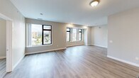 Located in Jackson, Michigan, this well-appointed 2-bedroom, 2-bathroom unit offers a thoughtfully designed single-floor layout with modern finishes throughout. Light-toned hardwood-style flooring flows seamlessly across the entire space, complementing the neutral warm-gray walls and clean white trim.

The open-concept kitchen and living area serves as the heart of the unit. The kitchen is equipped with stainless steel appliances, including a full-size refrigerator, electric range with microwave, and a deep double-basin sink. Crisp white shaker-style cabinetry pairs elegantly with dark granite countertops, while a subway tile backsplash adds a refined touch. A central island with pendant lighting provides additional prep space and seating.

The living area is generously proportioned, bathed in natural light from large picture windows that frame striking views of the downtown Jackson skyline.

Both bedrooms are comfortably sized with ample natural light. The primary bedroom connects to a private bathroom and a dedicated walk-in closet fitted with wire shelving for organized storage. The second bedroom also enjoys downtown views through a large window. Each bathroom features a tub-shower combination, with the primary bath including a white vanity with dark granite countertops and a mirrored cabinet.