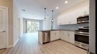 This thoughtfully designed single-floor residence offers a seamless blend of modern aesthetics and functional living. The open-concept kitchen and living area serves as the heart of the home, bathed in natural light from large sliding glass doors that open to a private balcony with lush tree views. The kitchen is outfitted with crisp white shaker-style cabinetry, dark countertops, a distinctive light blue hexagonal tile backsplash, and a full suite of stainless steel appliances including a gas range, built-in microwave, dishwasher, and refrigerator. Pendant lighting over the peninsula adds a warm, modern touch. Light-toned luxury vinyl plank flooring flows consistently throughout the space, enhancing the bright and airy atmosphere. A dedicated home office area features built-in shelving and a desk with integrated drawers, providing a practical workspace. The primary bathroom includes a glass-enclosed walk-in shower with full subway tile surround, while a second full bathroom offers a soaking tub and shower combination, a white vanity with dark countertop, and a backlit mirror. Bedrooms are well-proportioned with large windows that frame views of surrounding greenery, completing this clean and contemporary living space.