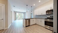 This thoughtfully designed single-floor residence offers a seamless blend of modern aesthetics and functional living. The open-concept kitchen and living area serves as the heart of the home, bathed in natural light from large sliding glass doors that open to a private balcony with lush tree views. The kitchen is outfitted with crisp white shaker-style cabinetry, dark countertops, a distinctive light blue hexagonal tile backsplash, and a full suite of stainless steel appliances including a gas range, built-in microwave, dishwasher, and refrigerator. Pendant lighting over the peninsula adds a warm, modern touch. Light-toned luxury vinyl plank flooring flows consistently throughout the space, enhancing the bright and airy atmosphere. A dedicated home office area features built-in shelving and a desk with integrated drawers, providing a practical workspace. The primary bathroom includes a glass-enclosed walk-in shower with full subway tile surround, while a second full bathroom offers a soaking tub and shower combination, a white vanity with dark countertop, and a backlit mirror. Bedrooms are well-proportioned with large windows that frame views of surrounding greenery, completing this clean and contemporary living space.
