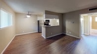 This single-floor, one-bedroom, one-bathroom unit offers a well-organized layout designed to maximize functionality. Rich, dark wood-style flooring runs consistently throughout the main living areas and bedroom, providing a cohesive visual foundation. The open living area is a standout feature, highlighted by a painted exposed brick accent wall that adds character and texture to the space. A ceiling fan overhead contributes to airflow and comfort.

The kitchen is positioned at the heart of the unit, separated from the living area by a peninsula-style breakfast bar. White cabinetry with raised panel detailing extends to the ceiling, maximizing storage capacity. Stainless steel appliances, including a refrigerator and range, are complemented by a black microwave, offering a functional cooking environment. The kitchen flooring transitions to a lighter wood-style finish.

The bedroom is a well-proportioned, private retreat with its own ceiling fan and a large window that welcomes natural light and provides an outdoor view. Neutral beige walls throughout the unit create a calm, versatile backdrop.

The bathroom includes a full tub-shower combination enclosed by earth-toned ceramic tile surround, with a small window above providing natural ventilation and light. White fixtures complete the clean, practical design of the space.