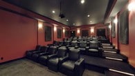 This single-floor screening room in Jefferson is designed to deliver an immersive, cinema-quality experience from the comfort of a private setting. The theater features multiple rows of tiered, stadium-style seating arranged to ensure unobstructed sightlines from every position. Each seat is a generously sized leather recliner equipped with built-in cup holders, providing both comfort and convenience during extended viewing sessions.

The room is finished with deep red walls that contribute to a classic, intimate theater ambiance, while dark ceiling treatment minimizes light reflection and enhances contrast during screenings. Acoustic wall panels are strategically placed throughout the space, optimizing sound absorption and reducing unwanted echo for a clear, high-fidelity audio experience.

Warm sconce lighting is mounted along the walls, offering a soft, adjustable glow that complements the dramatic atmosphere without interfering with the viewing environment. Recessed ceiling lights provide additional illumination when needed. A ceiling-mounted projector anchors the room's high-performance audio-visual setup. Carpeted flooring throughout adds to the acoustic performance while enhancing comfort underfoot. This thoughtfully designed theater space offers a professional-grade cinematic environment suited for both film enthusiasts and entertaining guests.