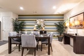 This single-floor residence in Marietta, Georgia offers a thoughtfully designed interior with a cohesive contemporary aesthetic carried throughout each room. The living room serves as a central gathering space, featuring plush carpeting, a bold teal and olive accent wall, large windows with grommet-panel drapes that invite natural light, and an exterior door providing convenient outdoor access.

The kitchen is equipped with warm honey-toned cabinetry, dark hardwood-style flooring, black appliances including a refrigerator, range, and dishwasher, and a pass-through bar connecting it to the main living area. Bar-height seating at the counter enhances the open feel between the kitchen and living spaces.

The dining area makes a strong visual statement with boldly striped multi-tone walls, plush carpeting, and ample room for a full dining set. Both bedrooms feature soft carpeting, large windows, accent walls in rich teal hues, and walk-in closet access. The primary bedroom includes a sitting area and an en-suite bath.

The bathrooms are finished with stone-look tile flooring, tub-shower combinations, and clean white fixtures. Modern decorative shelving adds functional style to each bath.