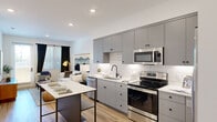 Located at 453 N McDowell Blvd in Petaluma, CA, this thoughtfully designed one-bedroom, two-bathroom residence offers a comfortable and modern living experience across a single floor. The open-concept layout connects the kitchen and living areas seamlessly, creating a bright and functional space ideal for both everyday living and entertaining.

The kitchen is a standout feature, showcasing sleek gray cabinetry, white subway tile backsplash, white quartz countertops, and a full suite of stainless steel appliances including a range, microwave, dishwasher, and French door refrigerator. A freestanding island with a dark metal frame provides additional prep and dining space. Light wood-style flooring runs throughout, complementing the clean, contemporary aesthetic.

The living room is generously proportioned, with natural light filtering in through large windows dressed with blinds and curtains. A secondary living area offers flexible use as a home office or study nook. The primary bedroom is a well-sized retreat with multiple windows, sheer curtains, and a dedicated walk-in closet outfitted with shelving and hanging rods. Both bathrooms are clean and modern, with white vanities, matte black fixtures, and tub-shower combinations. Recessed lighting throughout enhances the bright, airy ambiance of this well-appointed home.