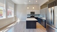 This single-floor unit at 1685 Elmwood Ave in Buffalo, New York, offers a thoughtfully designed modern interior with clean lines and high-quality finishes throughout. The open-concept kitchen serves as a central feature, showcasing two-tone cabinetry with dark lower cabinets and crisp white upper cabinets, complemented by a blue-gray mosaic tile backsplash. A central island with a white quartz-style countertop provides additional workspace, while stainless steel appliances—including a range, microwave, and dishwasher—add a polished, functional touch. Pendant lighting above the island and recessed ceiling lights ensure the space is well-illuminated.

Light hardwood flooring runs consistently throughout the living areas and bedrooms, contributing to a bright, cohesive aesthetic. The living space is generously sized with neutral gray walls and features a distinctive arched architectural detail. A bedroom includes a transom-style interior window that borrows light from an adjoining space, adding an interesting design element while keeping the room feeling open.

The bathroom is finished with large-format neutral floor tiles, a dark espresso vanity with a clean white countertop, and a walk-in shower enclosed by sliding glass doors and fully tiled in white subway tile, creating a spa-like atmosphere. Overall, the unit presents a contemporary and well-appointed living environment.