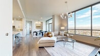 This thoughtfully designed 3-bedroom, 5-bathroom residence delivers an elevated living experience across a single, generously proportioned floor. The open-concept living and dining area is anchored by dramatic floor-to-ceiling windows that frame sweeping panoramic views of the surrounding cityscape and distant mountains, flooding the space with natural light. Wide-plank hardwood flooring flows throughout, complemented by a stylish chandelier and a large sectional seating area ideal for relaxing or entertaining. The dining room connects seamlessly to a private balcony, offering an effortless indoor-outdoor experience. The gourmet kitchen is a standout feature, showcasing white shaker cabinetry with matte black hardware, a herringbone tile backsplash, quartz countertops, and a professional-grade stainless steel range. A dedicated office with a sliding barn door provides a versatile private workspace. The spacious primary bedroom suite includes a well-appointed ensuite bathroom with dual vanities and tile flooring, alongside a custom walk-in closet with built-in shelving and drawers. A full-size laundry room with ample cabinetry and a utility sink adds everyday convenience. With hallways accented by coffered ceiling details and abundant storage throughout eight closets, this residence balances refined design with practical functionality.