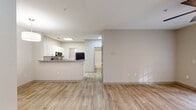 This single-story unit is designed with a clean, contemporary aesthetic, characterized by light wood-style flooring and soft neutral tones that flow consistently throughout every room. The open-concept living area is spacious and well-lit, benefiting from recessed lighting and natural light filtering in through windows. A ceiling fan is installed in one of the rooms, adding both function and a finishing detail to the space.

The kitchen is a notable feature, outfitted with white cabinetry, granite-style countertops, and a full suite of stainless steel appliances including a refrigerator, range, over-the-range microwave, and dishwasher. A peninsula with an undermount sink provides additional prep space and serves as a natural divider between the kitchen and living areas. A skylight above the kitchen enhances brightness in this central space.

Adjacent rooms offer flexible use, each with consistent flooring and neutral wall tones. The bathroom is finished with a granite-top vanity, tiled tub-shower combination, and the same wood-style flooring found throughout the unit. A panel-style entry door opens into the living area, alongside a secondary interior door, providing practical access throughout the layout. Overall, the unit presents a tidy, move-in-ready environment with cohesive finishes.