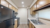 This single-floor, 3-bedroom, 1-bathroom unit offers a practical and well-organized layout designed to maximize every square foot. The galley-style kitchen is efficiently arranged with warm wood-toned cabinetry lining both walls, light-colored countertops, a double stainless steel sink, and black appliances including a refrigerator and range with overhead ventilation. Recessed lighting and light wood-look flooring give the kitchen a clean, functional feel.

The living area transitions seamlessly from the kitchen and features neutral carpet, textured ceilings, and a front entry door with an adjacent window fitted with horizontal blinds, allowing for natural light. The three bedrooms are carpeted and finished in warm beige tones, each featuring windows with blinds that bring in outdoor views and natural light. The spacious primary bedroom includes a ceiling fan and a generous footprint, while the additional bedrooms offer closet access and windows with exterior views.

The bathroom is finished with wood-toned cabinetry, a light countertop vanity, wood-look vinyl flooring, and includes a shower/tub combination. A hallway connects the main living spaces to the bedrooms and bathroom, contributing to the unit's cohesive and navigable floor plan. Overall, the space presents a neutral, move-in-ready aesthetic throughout.