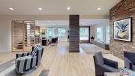 Located in Silverdale, Washington, this single-story community clubhouse offers a thoughtfully designed amenity space built for both relaxation and entertainment. The open-plan layout flows seamlessly between distinct zones, each with its own character and purpose.

At the heart of the space, a stylish lounge area anchors the room with woven pendant lighting, a sleek linear fireplace framed by built-in shelving, and light hardwood flooring. Adjacent to this, a well-appointed refreshment station with dark cabinetry provides a convenient beverage area for residents.

The game room is a standout feature, boasting a full-size billiards table set atop rich terracotta-hued carpeting, arcade machines, and a foosball table — all surrounded by boldly striped accent walls in navy, gold, and white. A separate lounge nook with leather sofas and a glowing "Game On" neon sign completes the entertainment atmosphere.

A dedicated workspace area features a large desk, task seating, and a wooden slatted partition divider set against an exposed brick accent wall, creating a semi-private environment ideal for focused work. The reception and entry zone is anchored by a distinctive stone-clad column and benefits from abundant natural light streaming through multiple windows, offering views of the surrounding greenery. Throughout, the design balances modern finishes with warm, inviting textures.