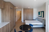 Located at 1629 Veteran Ave in the Westwood neighborhood of Los Angeles, this single-floor unit showcases a clean, modern aesthetic throughout. The living area features light hardwood flooring, a wall-mounted mini-split climate control system, and a built-in desk workspace, creating a functional and stylish environment. Contemporary artwork adorns the white walls, adding a curated touch to the space.

The bedrooms are bright and thoughtfully designed, with one featuring floor-to-ceiling warm wood sliding wardrobe doors that provide generous storage. Natural light filters through windows, and each bedroom is equipped with adjustable wall-mounted reading lamps for added convenience.

The bathrooms maintain the same clean, minimalist palette, finished with large-format light gray tiles. One bathroom includes a glass-enclosed walk-in shower with a built-in niche, mosaic tile flooring, and a sleek chrome fixture system. A second bathroom features a compact, well-organized layout with wood cabinetry.

A dedicated laundry room houses two stacked washer and dryer units, offering a practical and space-efficient solution. Throughout the unit, the consistent use of neutral tones, natural wood accents, and recessed lighting creates a cohesive, contemporary ambiance well-suited to modern urban living.