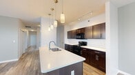 Located at 610 Elizabeth St in Mishawaka, Indiana, this single-floor unit offers a thoughtfully designed layout with contemporary finishes throughout. Wood-look plank flooring runs consistently across the living areas, bedrooms, and bathrooms, contributing to a cohesive and clean aesthetic.

The kitchen serves as a central feature of the space, showcasing rich dark-espresso cabinetry paired with crisp white quartz countertops. A spacious island with an undermount sink anchors the kitchen, illuminated by a series of pendant lights suspended from above. Track lighting along the ceiling provides additional task lighting, while black appliances including a range, microwave, and refrigerator complete the functional setup.

The living area is bright and open, benefiting from multiple windows and a sliding glass door that invites natural light and outdoor views. Neutral gray walls complement the light flooring and create a calm, versatile backdrop throughout the space.

The bedrooms are well-proportioned, each featuring natural light from windows and sliding closet doors with built-in shelving for organized storage. The bathroom includes a tub-shower combination with glass enclosure, a dark vanity with white countertop, and clean, neutral finishes. A separate water closet configuration is also present, enhancing functionality and privacy.