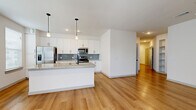 This single-floor residence offers a comfortable and efficiently designed layout across two bedrooms and two bathrooms. The open-concept kitchen and living area serves as the heart of the home, showcasing warm light wood-tone flooring, recessed lighting, and pendant lights above a granite-topped island. The kitchen is equipped with stainless steel appliances, white shaker-style cabinetry, a blue-gray subway tile backsplash, and ample counter space, creating a clean, modern aesthetic. A door with a sidelight panel in the living area provides access to the outdoors and brings in natural light.

The bedrooms are carpeted for comfort, with the primary bedroom featuring dual windows with blinds, a ceiling fan, and direct access to a spacious walk-in closet fitted with wire shelving. The second bedroom is similarly carpeted and connects to a closet as well. Both bathrooms are finished with large-format tile flooring, granite vanity countertops, white cabinetry with matte black hardware, and glass-enclosed showers. The overall palette throughout the residence is neutral and bright, contributing to a clean, contemporary feel.