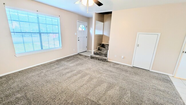 Carpeted living room with large picture window, tiled entry, and stairway access. - 813 Clubside Dr