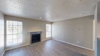 This single-floor space is designed with a neutral, contemporary palette throughout, creating a cohesive and move-in-ready atmosphere. The living room serves as the centerpiece, showcasing wood-look laminate flooring, a textured popcorn ceiling, and a tiled fireplace with a white mantel as a focal point. Multiple windows allow natural light to fill the room from several angles, enhancing the open and airy feel of the space.

Adjacent to the living area, the galley-style kitchen is efficiently laid out with gray cabinetry lining both walls, gray laminate countertops, a double stainless steel sink, and a white electric range with an overhead exhaust hood. Light wood-look tile flooring ties the kitchen together cleanly, and a door at the end provides additional access.

The bedrooms feature wall-to-wall carpet and ceiling fans with integrated lighting, contributing to a comfortable and functional environment. One bedroom includes two closet doors, offering practical storage. A secondary room with carpet and a ceiling fan also includes a glass-paned exterior door, bringing in additional natural light and outdoor access.

The bathroom is straightforward and functional, equipped with a full tub-shower combination, toilet, and vanity with light wood-look flooring completing the space.