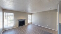 This single-floor space is designed with a neutral, contemporary palette throughout, creating a cohesive and move-in-ready atmosphere. The living room serves as the centerpiece, showcasing wood-look laminate flooring, a textured popcorn ceiling, and a tiled fireplace with a white mantel as a focal point. Multiple windows allow natural light to fill the room from several angles, enhancing the open and airy feel of the space.

Adjacent to the living area, the galley-style kitchen is efficiently laid out with gray cabinetry lining both walls, gray laminate countertops, a double stainless steel sink, and a white electric range with an overhead exhaust hood. Light wood-look tile flooring ties the kitchen together cleanly, and a door at the end provides additional access.

The bedrooms feature wall-to-wall carpet and ceiling fans with integrated lighting, contributing to a comfortable and functional environment. One bedroom includes two closet doors, offering practical storage. A secondary room with carpet and a ceiling fan also includes a glass-paned exterior door, bringing in additional natural light and outdoor access.

The bathroom is straightforward and functional, equipped with a full tub-shower combination, toilet, and vanity with light wood-look flooring completing the space.