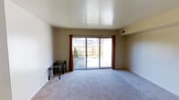 This two-story space offers a well-organized layout designed for comfortable everyday living. The main living area is a standout feature, highlighted by large sliding glass doors dressed with rich red curtains that flood the room with natural light and provide direct access to an outdoor patio. The space beyond the doors reveals a private exterior area with surrounding greenery, offering a pleasant outdoor retreat. The living area is finished with soft, plush wall-to-wall carpeting in a neutral tone, contributing to a warm and inviting atmosphere. Smooth, clean ceilings and neutral-toned walls throughout create a versatile backdrop that suits a variety of interior styles. The open feel of the main living space is enhanced by its generous proportions, making it ideal for both relaxing and entertaining. Subtle architectural details, including a recessed wall niche, add a touch of character to the interior. Spread across two floors, the layout provides a natural separation between living and private spaces, offering both functionality and a sense of defined zones within the home. Overall, the space balances simplicity with practicality in a clean, well-maintained environment.
