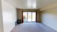 This two-story space offers a well-organized layout designed for comfortable everyday living. The main living area is a standout feature, highlighted by large sliding glass doors dressed with rich red curtains that flood the room with natural light and provide direct access to an outdoor patio. The space beyond the doors reveals a private exterior area with surrounding greenery, offering a pleasant outdoor retreat. The living area is finished with soft, plush wall-to-wall carpeting in a neutral tone, contributing to a warm and inviting atmosphere. Smooth, clean ceilings and neutral-toned walls throughout create a versatile backdrop that suits a variety of interior styles. The open feel of the main living space is enhanced by its generous proportions, making it ideal for both relaxing and entertaining. Subtle architectural details, including a recessed wall niche, add a touch of character to the interior. Spread across two floors, the layout provides a natural separation between living and private spaces, offering both functionality and a sense of defined zones within the home. Overall, the space balances simplicity with practicality in a clean, well-maintained environment.