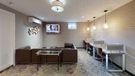 The Club Room at 304 S Second Ave in Highland Park, NJ is a thoughtfully designed amenity space that seamlessly blends comfort and functionality. The room features a cohesive, contemporary aesthetic with warm neutral tones, patterned wallcoverings, and a mix of recessed and pendant lighting that creates a welcoming ambiance throughout.

The lounge area serves as the centerpiece of the space, furnished with a tufted brown leather sectional sofa and coordinating chairs arranged around a glass-top coffee table. A wall-mounted flat-screen TV makes this area ideal for both relaxation and group viewing. An elegant decorative wall installation adds an artistic touch to the room.

Adjacent to the lounge, a dedicated co-working zone offers a long shared desk surface accompanied by individual pendant lights and ergonomic seating, providing a productive environment for residents who need a quiet workspace.

The wet bar area is outfitted with dark espresso cabinetry, granite countertops, and an undermount sink, all topped by a pair of framed abstract artworks that lend a refined, gallery-like quality to the space. A wall-mounted mini-split HVAC unit ensures year-round climate comfort.

The flooring throughout features a patterned area rug layered over tile, tying together the various zones cohesively. A small window provides a touch of natural light, complementing the well-appointed interior lighting.