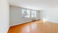 Located at 9503 State Rd in Philadelphia's 19114 neighborhood, this efficiently designed single-floor unit makes excellent use of its compact footprint. The open-concept kitchen and living area form the heart of the space, finished with warm honey-toned hardwood flooring that extends throughout. The kitchen is thoughtfully appointed with white upper cabinetry, two-tone gray lower cabinets, white countertops, and a classic subway tile backsplash. Black appliances — including a full-size refrigerator, electric range, built-in microwave, and dishwasher — provide a bold contrast against the light cabinetry. A flush ceiling light fixture brightens the kitchen area. The living space is bathed in natural light streaming through two large windows that frame outdoor greenery, creating a bright and airy atmosphere. A wall-mounted HVAC unit ensures year-round comfort. A closet with bifold doors offers practical storage. The bathroom features neutral tile flooring, a full soaking tub and shower combo with beige tile surround, a vanity with storage, and clean white walls that give the space a crisp, functional feel. Overall, the unit presents a clean, modern aesthetic with a neutral palette throughout.