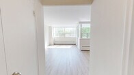 Located at 4415 Bathurst Street in Toronto's North York neighbourhood, this one-bedroom, one-bathroom unit offers a well-organized layout across a single floor. Light wood laminate flooring flows throughout the living areas, complementing the clean, neutral palette of white and soft grey tones on the walls.

The living room is generously proportioned, bathed in natural light through large, floor-to-ceiling windows that frame lush treetop views of the surrounding greenery. Baseboard heating runs along the window walls, and a door leads to an enclosed sunroom-style nook, further expanding the sense of space and providing additional exposure to natural light.

The bedroom is a comfortable size, featuring its own set of wide windows that invite natural light and offer pleasant outdoor views. The kitchen is functional and well-appointed, with white cabinetry, dark laminate countertops, a double-basin stainless steel sink, and a tiled backsplash providing ample storage and workspace.

The bathroom is finished with warm-toned tile flooring, a white vanity with storage, a full soaker tub with a shower curtain enclosure, and wall sconce lighting. An entrance foyer and hallway connect the rooms efficiently, completing this bright and practical urban residence.