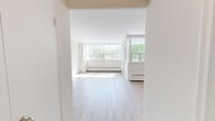 Located at 4415 Bathurst Street in Toronto's North York neighbourhood, this one-bedroom, one-bathroom unit offers a well-organized layout across a single floor. Light wood laminate flooring flows throughout the living areas, complementing the clean, neutral palette of white and soft grey tones on the walls.

The living room is generously proportioned, bathed in natural light through large, floor-to-ceiling windows that frame lush treetop views of the surrounding greenery. Baseboard heating runs along the window walls, and a door leads to an enclosed sunroom-style nook, further expanding the sense of space and providing additional exposure to natural light.

The bedroom is a comfortable size, featuring its own set of wide windows that invite natural light and offer pleasant outdoor views. The kitchen is functional and well-appointed, with white cabinetry, dark laminate countertops, a double-basin stainless steel sink, and a tiled backsplash providing ample storage and workspace.

The bathroom is finished with warm-toned tile flooring, a white vanity with storage, a full soaker tub with a shower curtain enclosure, and wall sconce lighting. An entrance foyer and hallway connect the rooms efficiently, completing this bright and practical urban residence.