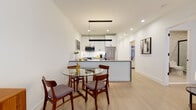 This well-appointed single-floor unit showcases a thoughtfully designed layout with modern finishes and a cohesive contemporary aesthetic throughout. Light hardwood flooring flows seamlessly across the main living areas, complemented by crisp white walls that enhance the sense of brightness and openness.

The open-concept kitchen is a standout feature, outfitted with sleek white cabinetry, marble-style backsplash, stainless steel appliances, and a peninsula with a matte black sink — ideal for both cooking and casual entertaining. A linear pendant light anchors the adjacent dining area, where a glass-top round table with mid-century style chairs creates an inviting space for meals.

The living room offers a relaxed, curated atmosphere with a tufted charcoal sofa, layered abstract wall art, and warm accent lighting. A separate sitting nook provides additional flexible space, complete with a tulip-style table and plush area rug.

The bedroom is serene and well-proportioned, featuring soft ambient lighting, art-accented walls, and a closet with clean black hardware details. The bathroom is finished with large-format tile flooring, textured wall tile, a warm wood vanity with black fixtures, and a combination tub and shower.

A dedicated office area with a large window overlooking surrounding brick architecture offers a productive, naturally lit workspace. The hallway utility area rounds out the functional layout of this well-designed unit.