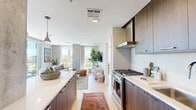 This well-appointed 2-bedroom, 2-bathroom residence offers a thoughtfully designed single-level layout with modern finishes throughout. The open-concept kitchen and living area serves as the heart of the home, where light hardwood floors and a neutral gray palette create a cohesive, contemporary feel. The kitchen is equipped with stainless steel appliances, including a gas range, French door refrigerator, built-in microwave, and dishwasher. Rich, dark wood cabinetry pairs with crisp white countertops, and a peninsula island with seating provides additional prep space and casual dining. Pendant lighting adds a stylish finishing touch overhead. The living room is bathed in natural light from expansive floor-to-ceiling windows that frame open outdoor views, creating an airy and inviting atmosphere. A distinctive exposed concrete structural column adds an industrial design element to the space. The primary bedroom is generously sized, offering comfortable accommodations, while the second bedroom provides flexible living space suitable for guests or a home office. Both bathrooms are finished with neutral large-format tile, with one featuring a deep soaking tub and shower combo with chrome fixtures. A well-lit hallway connects all rooms, completing this efficient and stylish layout.