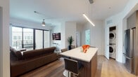 Located at 5211 Peachtree Blvd in Chamblee, Georgia, this contemporary single-floor residence showcases a clean, modern aesthetic with an open-concept design and light hardwood flooring throughout. The living area is bright and welcoming, anchored by floor-to-ceiling sliding glass doors that open onto a private balcony offering open views of the surrounding urban landscape. A ceiling fan adds comfort, while the seamless flow between spaces enhances the sense of openness.

The kitchen is well-appointed with flat-front cabinetry in a warm wood-tone finish, a white quartz countertop, a full suite of stainless steel appliances including a gas range, built-in microwave, and French door refrigerator, and a glass tile backsplash. A peninsula with bar-height seating provides an ideal casual dining or entertaining space, illuminated by a sleek linear pendant light.

The bedroom features large windows with vertical blinds allowing ample natural light, a ceiling fan, and a bold accent wall in charcoal gray that adds depth and character. The bathroom is appointed with crisp white finishes, large-format floor tiles, and a frameless glass walk-in shower with a rainfall showerhead. The overall design balances contemporary style with functional, comfortable living.